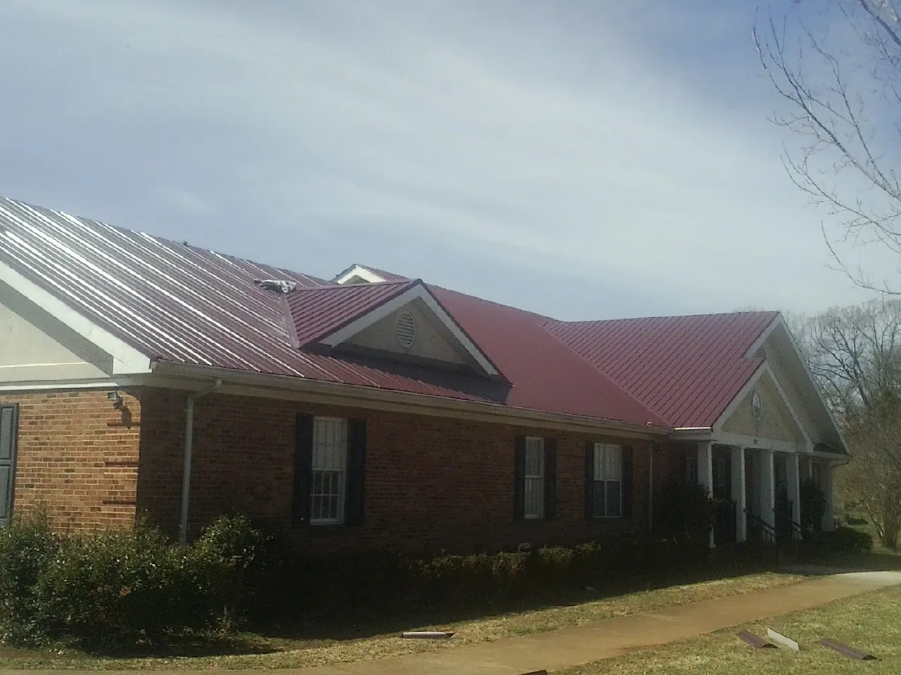 Red metal roof with gabled entries on a long brick building, from a Hail Damage Roof Repair job in Cross Anchor