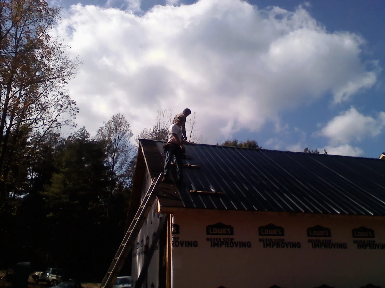 Roofer fastening dark metal panels high against a cloudy sky, from a Roof Inspection job in Cross Anchor