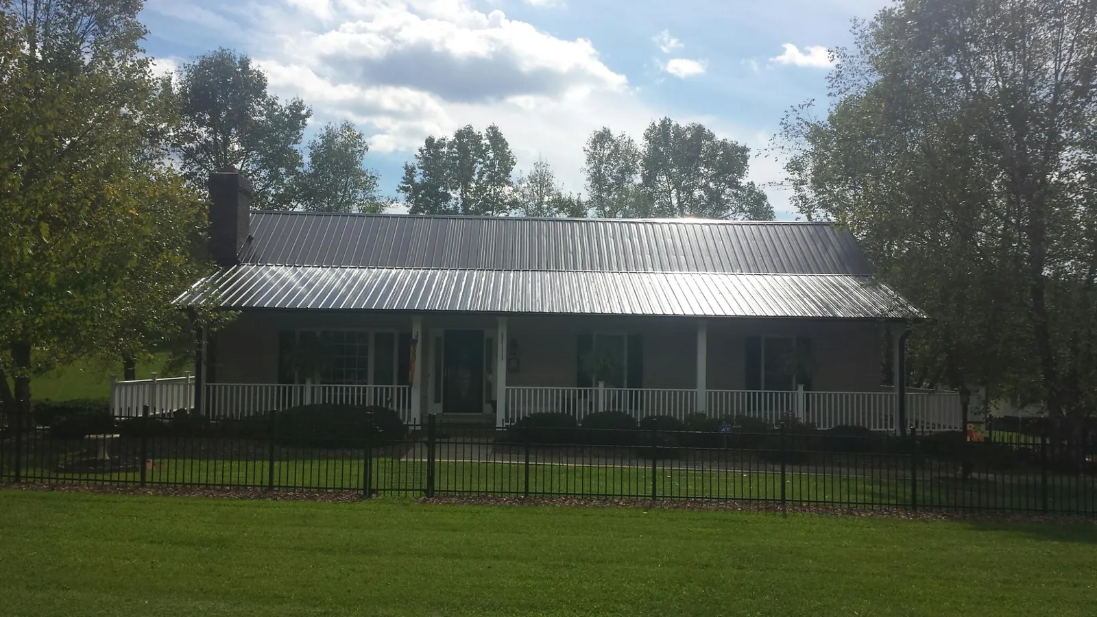 Gray metal roof on a brick ranch with a full width front porch — Gutter Guard Installation work by our crew in Cross Anchor