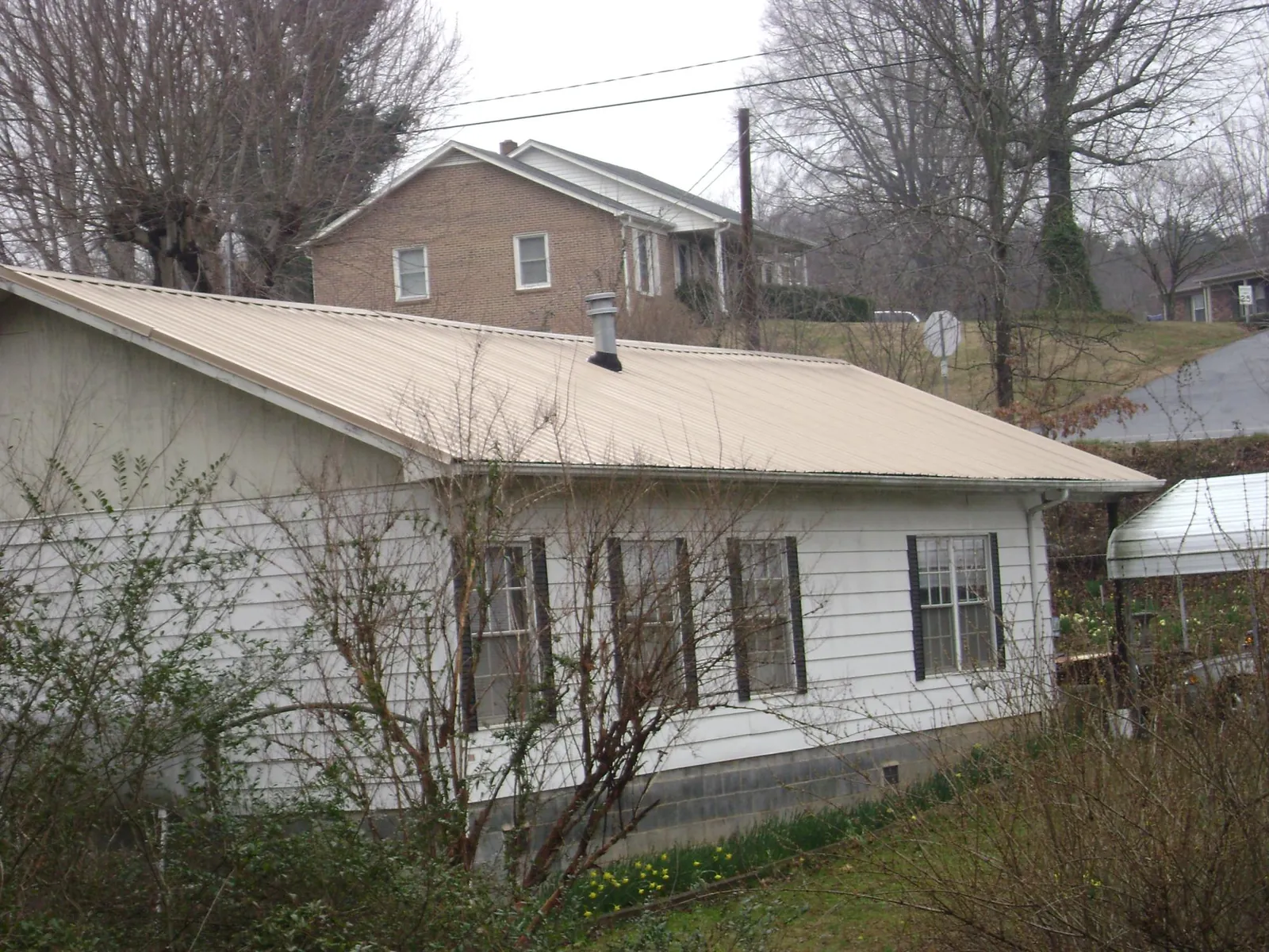 Tan metal roof on a white sided house set into a hillside — Commercial Roofing by Roofing Brothers in Cross Anchor