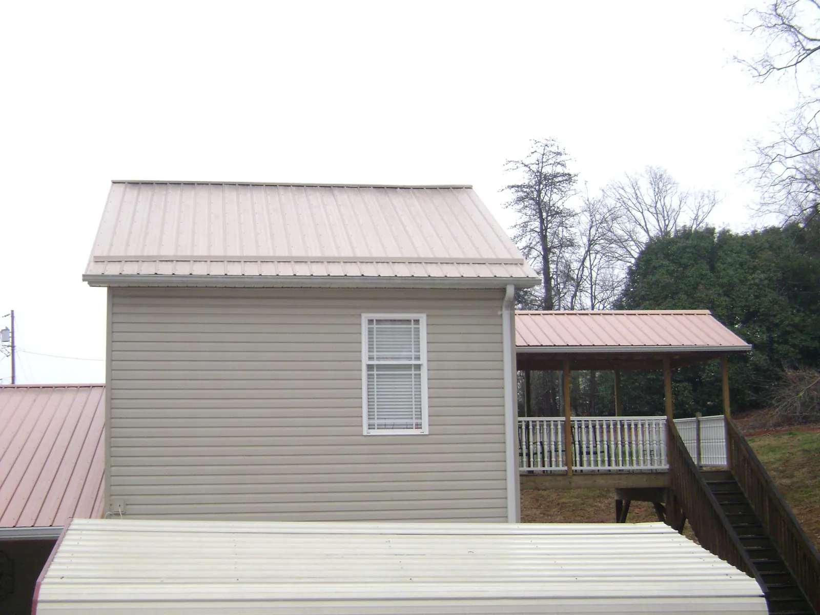 Tan metal roofs on a two story addition and attached porch, from a Roof Replacement job in Cross Anchor